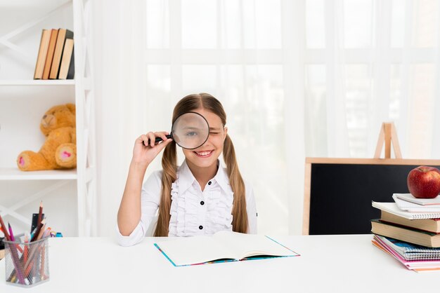 Colegiala inteligente mirando a través de la lupa