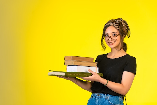 Foto gratuita colegiala joven en anteojos sosteniendo sus libros y sonriendo positivamente.