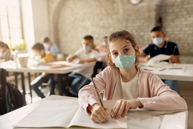 Colegiala con mascarilla protectora mientras aprende en el aula