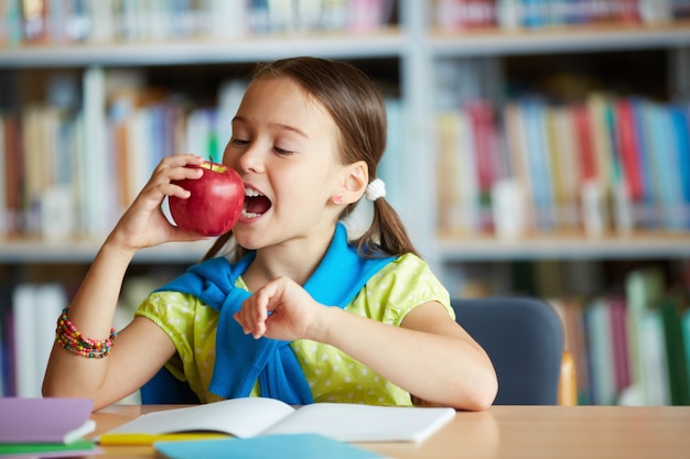 Foto gratuita colegiala mordiendo una manzana en la biblioteca