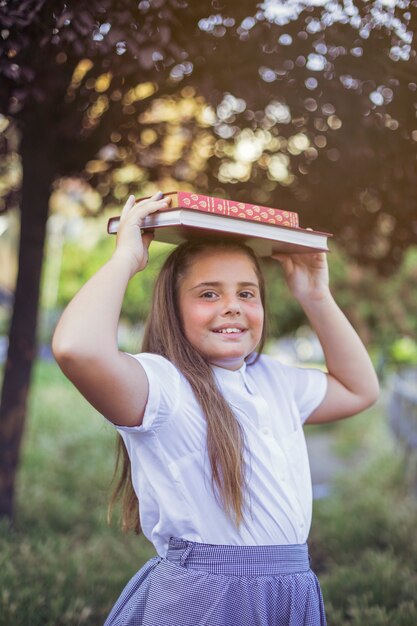 Colegiala de pie con libros en la cabeza sonriendo