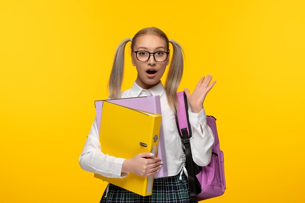 Colegiala rubia emocionada del día mundial del libro con las manos agitadas con gafas