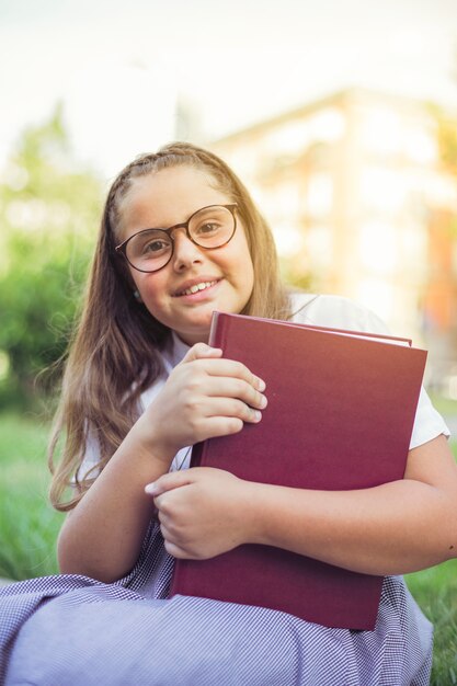 Colegiala sentada en la hierba con libro sonriendo