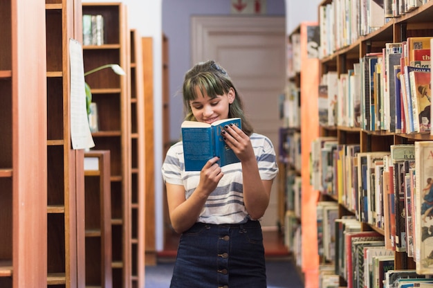 Colegiala sonriente leyendo un libro en la biblioteca