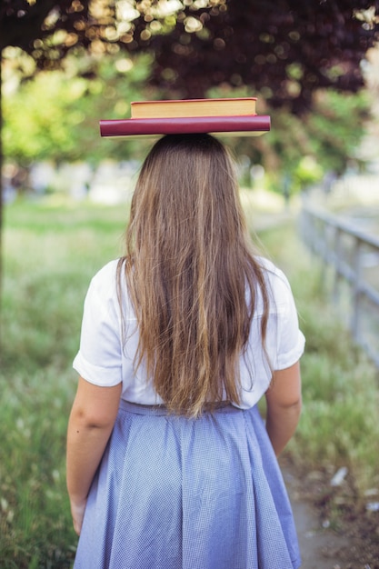 Foto gratuita colegiala en uniforme de pie en el jardín con el libro en la cabeza