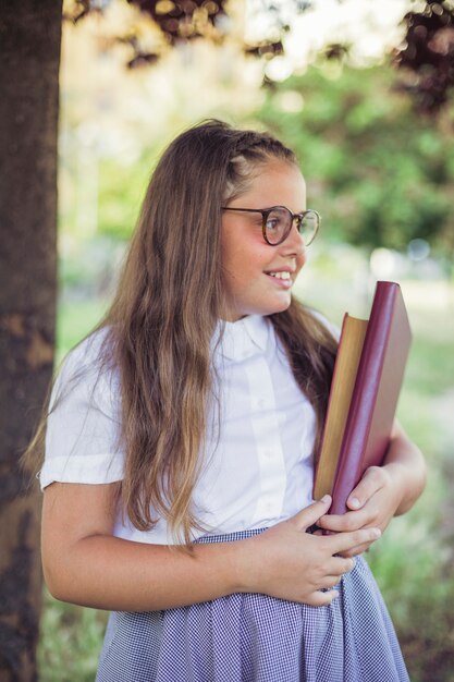 Colegiala en uniforme de pie en el jardín con libros