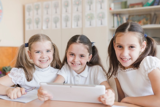 Colegialas alegres con tableta mirando la cámara