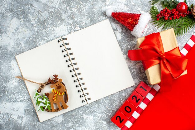 Colgante del árbol de navidad de la vista superior en bloques de madera del cuaderno pequeño sombrero de santa en la mesa blanca gris