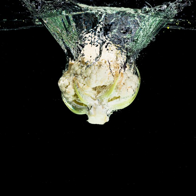 Coliflor caer al agua contra el fondo negro