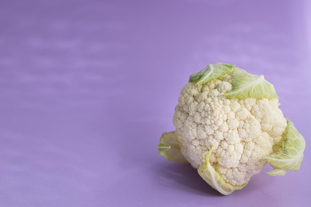 Coliflor fresca sobre un fondo morado con sombras duras, espacio de copia