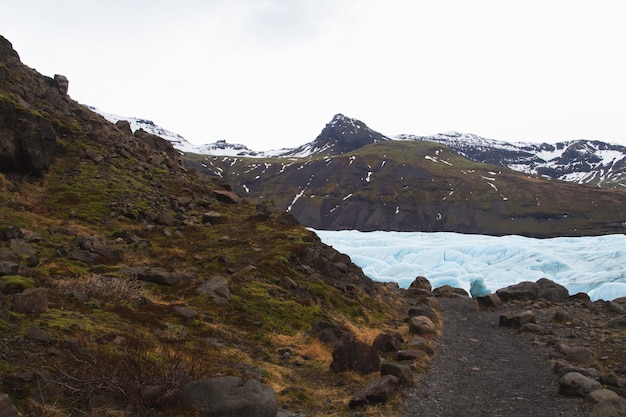 Colinas cubiertas de nieve y pasto rodeado por un lago congelado en el Parque Nacional Vatnajokull