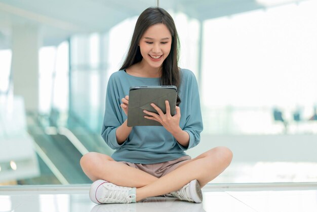 Collage femenino asiático mujer joven del campus sentada en el piso del centro comercial usando tableta navegando datos de navegación en las redes sociales en línea con alegre diversión sonriente mujer asiática nómada digital sentada en el piso trabajo informal en línea