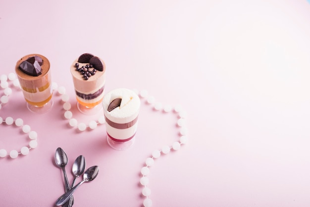 Collar de perlas blancas y cucharas cerca del pudín de chocolate y vainilla en copas.