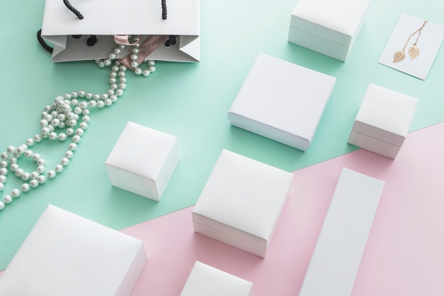 Collar de perlas blancas con diferentes cajas blancas sobre fondo de papel pastel