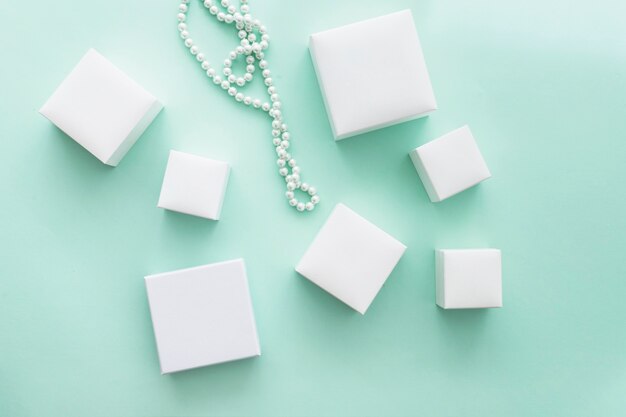 Collar de perlas con diferentes cajas blancas sobre fondo turquesa