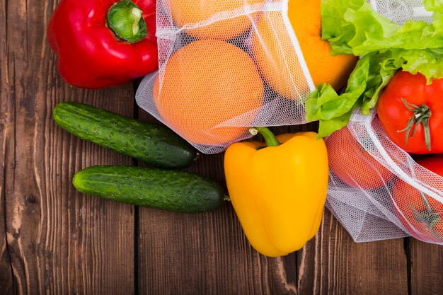 Colocación plana de bolsas reutilizables en superficie de madera con verduras y frutas.