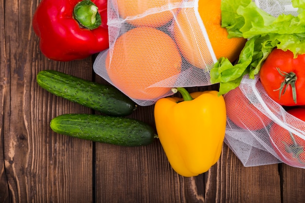 Colocación plana de bolsas reutilizables en superficie de madera con verduras y frutas.