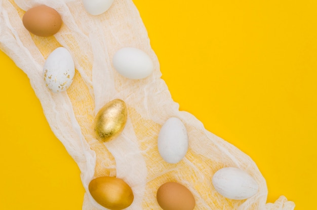 Foto gratuita colocación plana de huevos de pascua con pintura dorada y textil