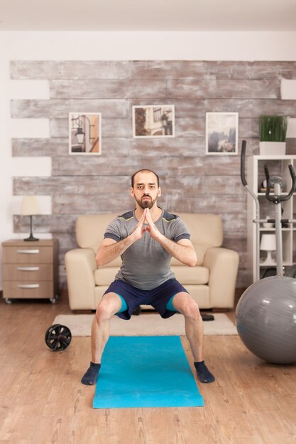 Colocar al hombre entrenando sus piernas en la estera de yoga durante la pandemia global.