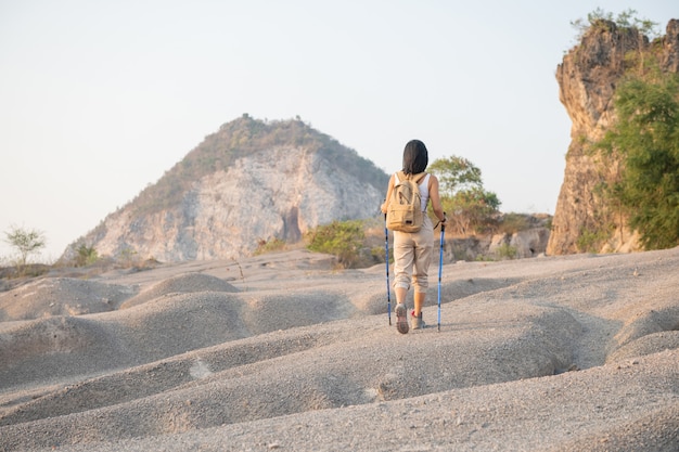 Colocar excursionista femenino con mochila y postes de pie en la cresta de la montaña rocosa mirando valles y picos.