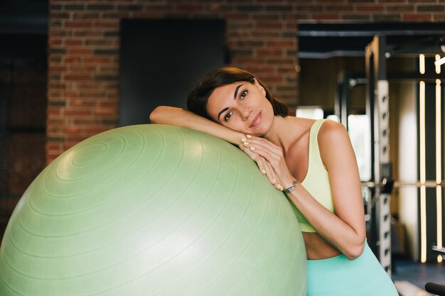 Colocar hermosa mujer caucásica en ropa deportiva adecuada en el gimnasio con fitball