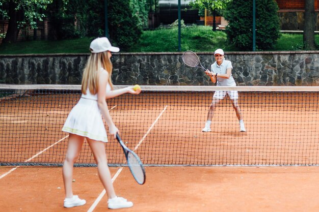 Colocar joven mujer con gorra y uniforme de tenis que sirve pelota de tenis durante el entrenamiento en la cancha de tenis al aire libre.