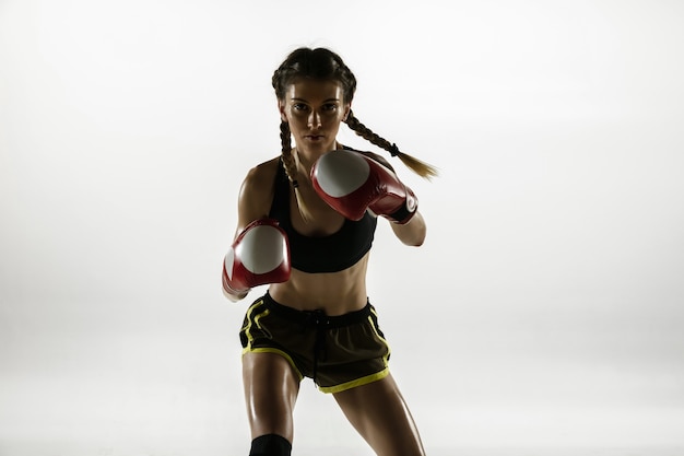 Colocar mujer caucásica en ropa deportiva de boxeo aislado en la pared blanca. Boxeador caucásico femenino novato entrenando y practicando en movimiento y acción. Deporte, estilo de vida saludable, concepto de movimiento.