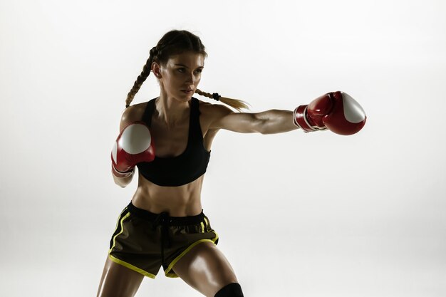 Colocar mujer caucásica en ropa deportiva de boxeo aislado en la pared blanca. Boxeador caucásico femenino novato entrenando y practicando en movimiento y acción. Deporte, estilo de vida saludable, concepto de movimiento.