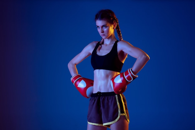 Colocar mujer caucásica en ropa deportiva de boxeo sobre fondo azul en luz de neón.