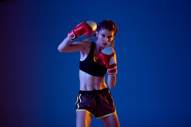 Colocar mujer caucásica en ropa deportiva de boxeo sobre fondo azul en luz de neón.