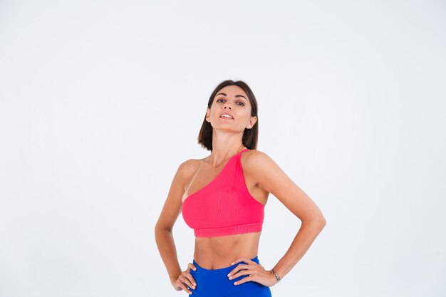 Colocar mujer deportiva bronceada con abdominales, curvas de fitness, vistiendo top y leggings azules sobre blanco