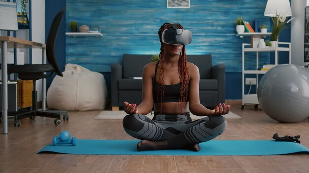 Colocar mujer negra con casco de realidad virtual mientras está sentado en el mapa de yoga