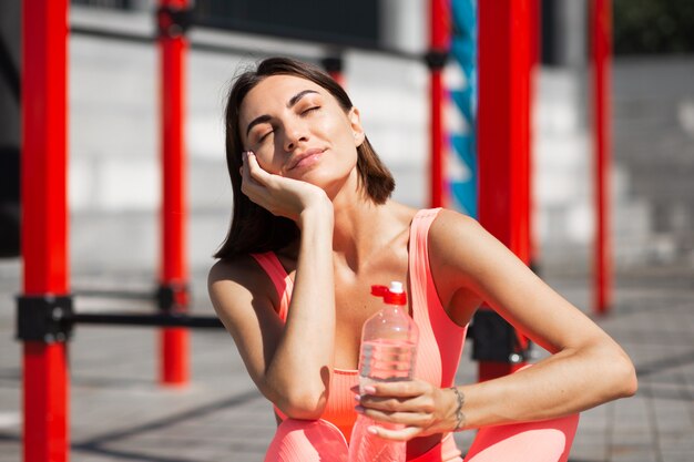 Colocar mujer en ropa deportiva de color rosa al aire libre con botella de agua