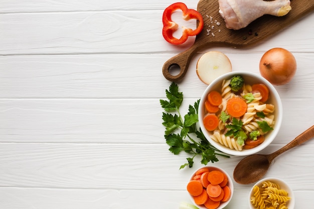 Foto gratuita coloque las zanahorias y el fusilli de brócoli en un tazón con muslo de pollo en la tabla de cortar con espacio de copia