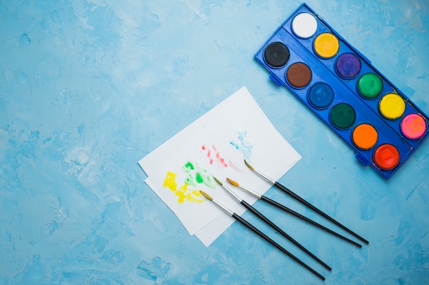 Color del agua teñido en papel blanco con pincel y paleta de colores sobre superficie azul