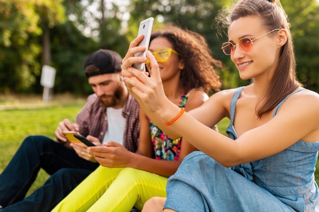 Colorida y elegante compañía joven feliz de amigos sentados en el parque, hombres y mujeres que se divierten juntos