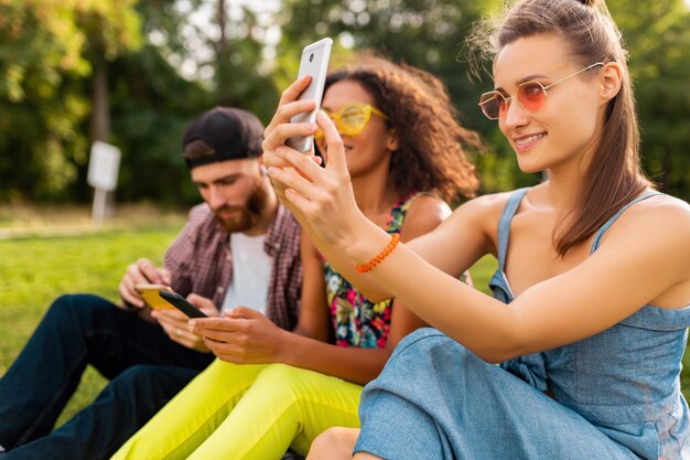 Colorida y elegante compañía joven feliz de amigos sentados en el parque, hombres y mujeres que se divierten juntos