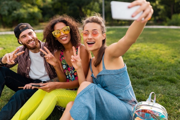 Colorida y elegante compañía joven feliz de amigos sentados en el parque, hombres y mujeres que se divierten juntos