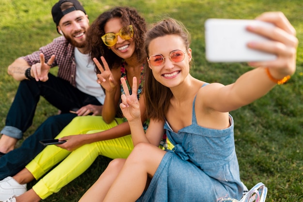 Colorida y elegante compañía joven feliz de amigos sentados en el parque, hombres y mujeres que se divierten juntos