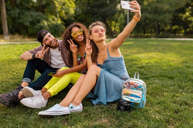 Colorida y elegante compañía joven feliz de amigos sentados en el parque, hombres y mujeres que se divierten juntos