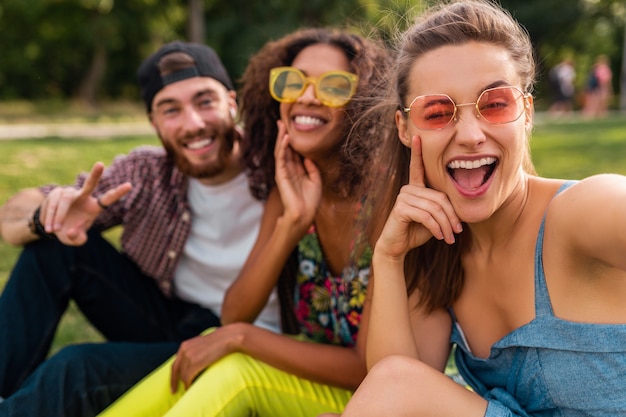 Foto gratuita colorida y elegante compañía joven feliz de amigos sentados en el parque, hombres y mujeres que se divierten juntos