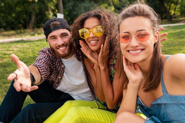 Colorida y elegante compañía joven feliz de amigos sentados en el parque, hombres y mujeres que se divierten juntos