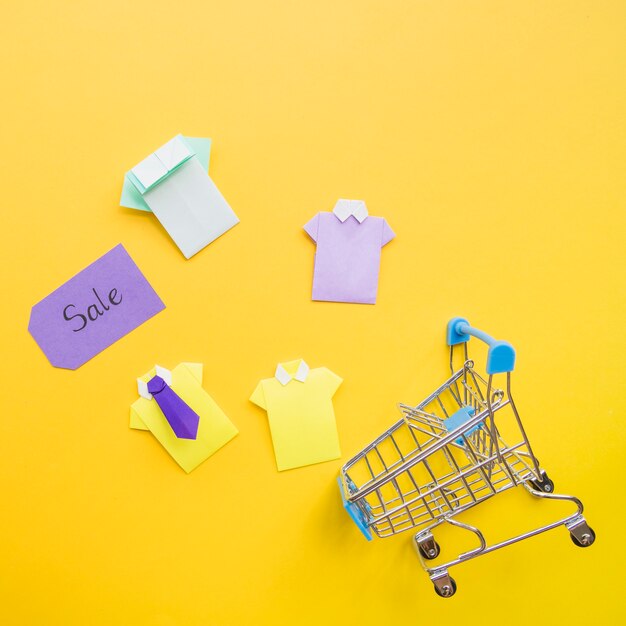 Coloridas camisas de papel de juguete cerca de carrito de compra y etiqueta de venta