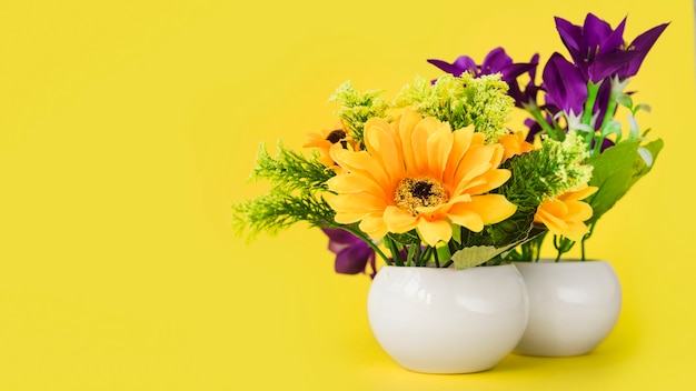 Coloridas flores en el pequeño jarrón blanco sobre fondo amarillo.