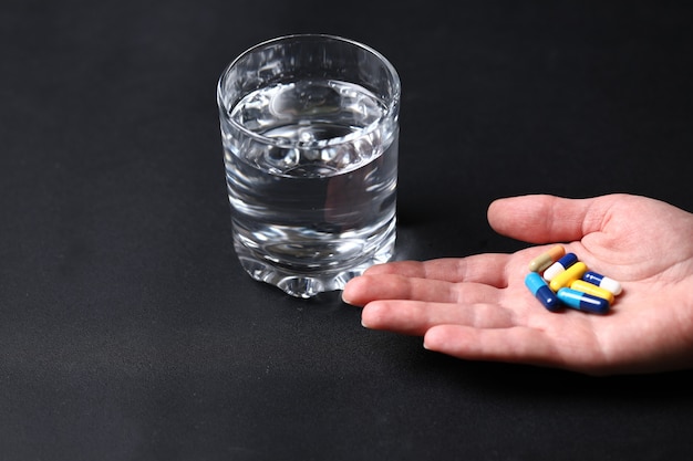 Coloridas píldoras médicas en la mano de una persona y un vaso de agua.