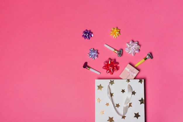 Colorido lazo de satén; caja de regalo y soplador de fiesta sobre la bolsa de papel sobre fondo rosa