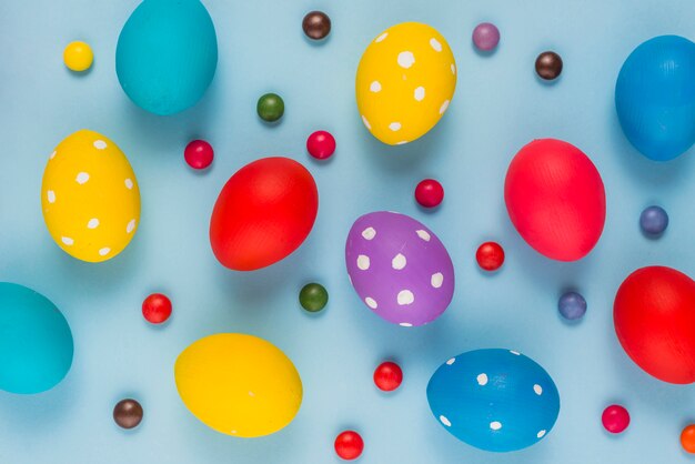Coloridos huevos de Pascua con caramelos en mesa azul