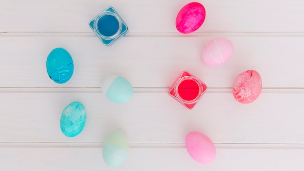 Coloridos huevos de Pascua cerca de latas de líquido tinte en el escritorio