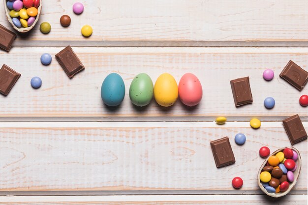 Coloridos huevos de Pascua con chocolate y gemas en el escritorio de madera