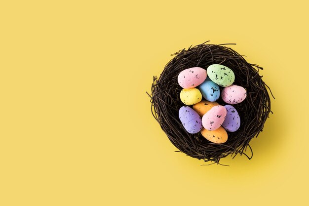 Coloridos huevos de Pascua dentro de un nido sobre fondo amarillo Copiar espacio